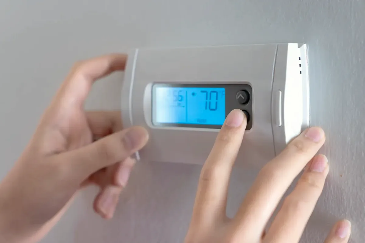 Hands adjusting a digital wall thermostat